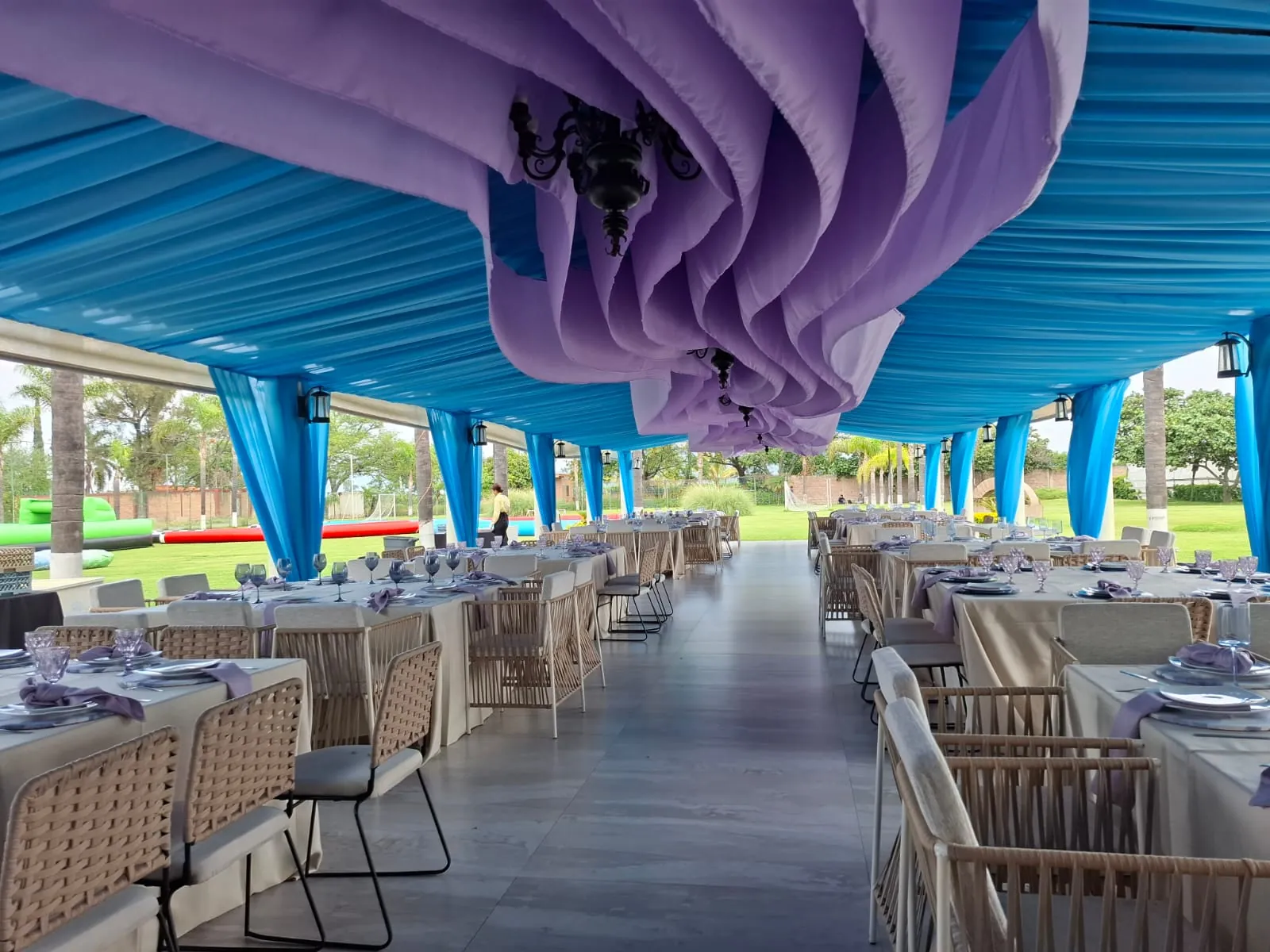 Techo de tela violeta y turquesa con candil sobre mesas de banquete al aire libre